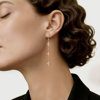 A pair of 18K yellow gold drop earrings with round-cut white diamonds, designed to resemble falling stars.